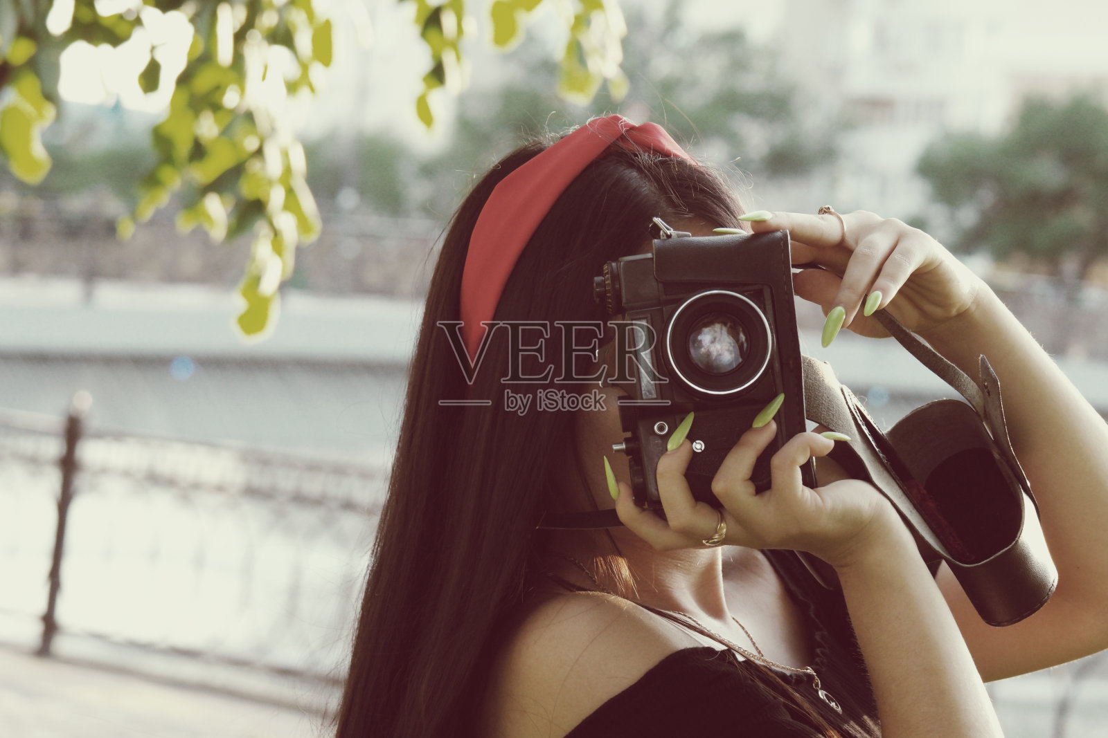 日落时分，带着相机的亚洲女孩在公园里。深色头发的女孩，带着老式胶卷相机照片摄影图片