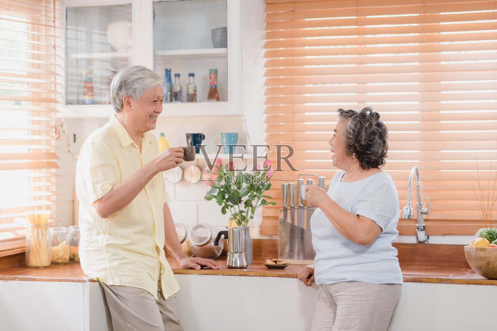 一对亚洲老夫妇在家里的厨房里喝着热咖啡，一起聊天。中国夫妇在家里一起享受爱的时刻。生活方式高级家庭居家理念。照片摄影图片
