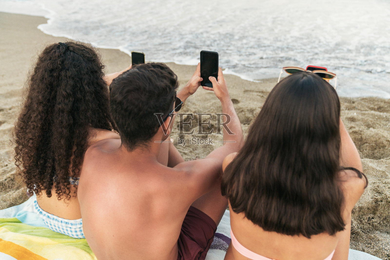 朋友们坐在沙滩上拿着智能手机照片摄影图片