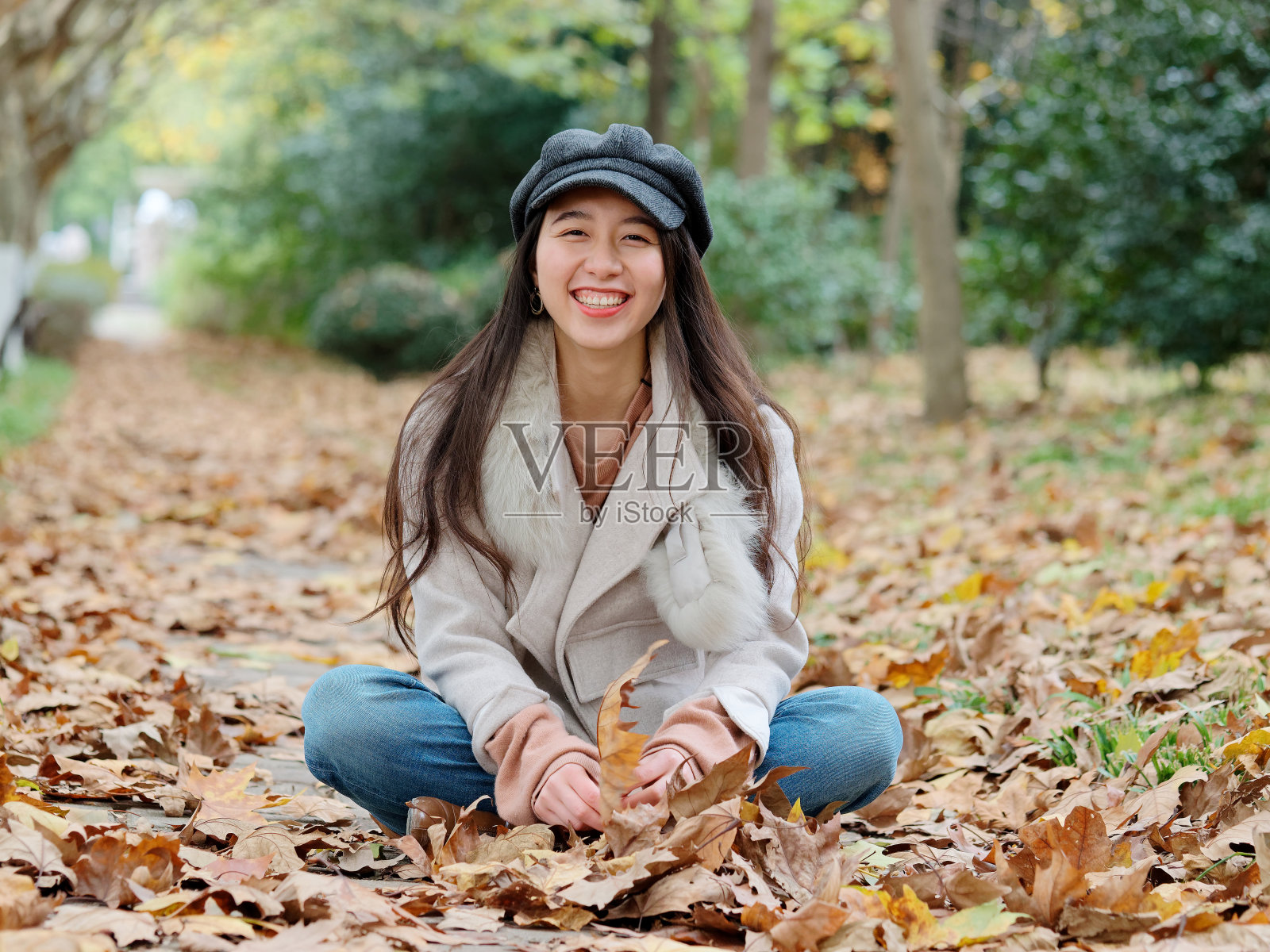 美丽的中国年轻女子的肖像穿着白色外套和牛仔裤坐在和微笑在秋天的公园，迷人的中国女孩与黑色的长发享受她的休闲时间的户外。照片摄影图片
