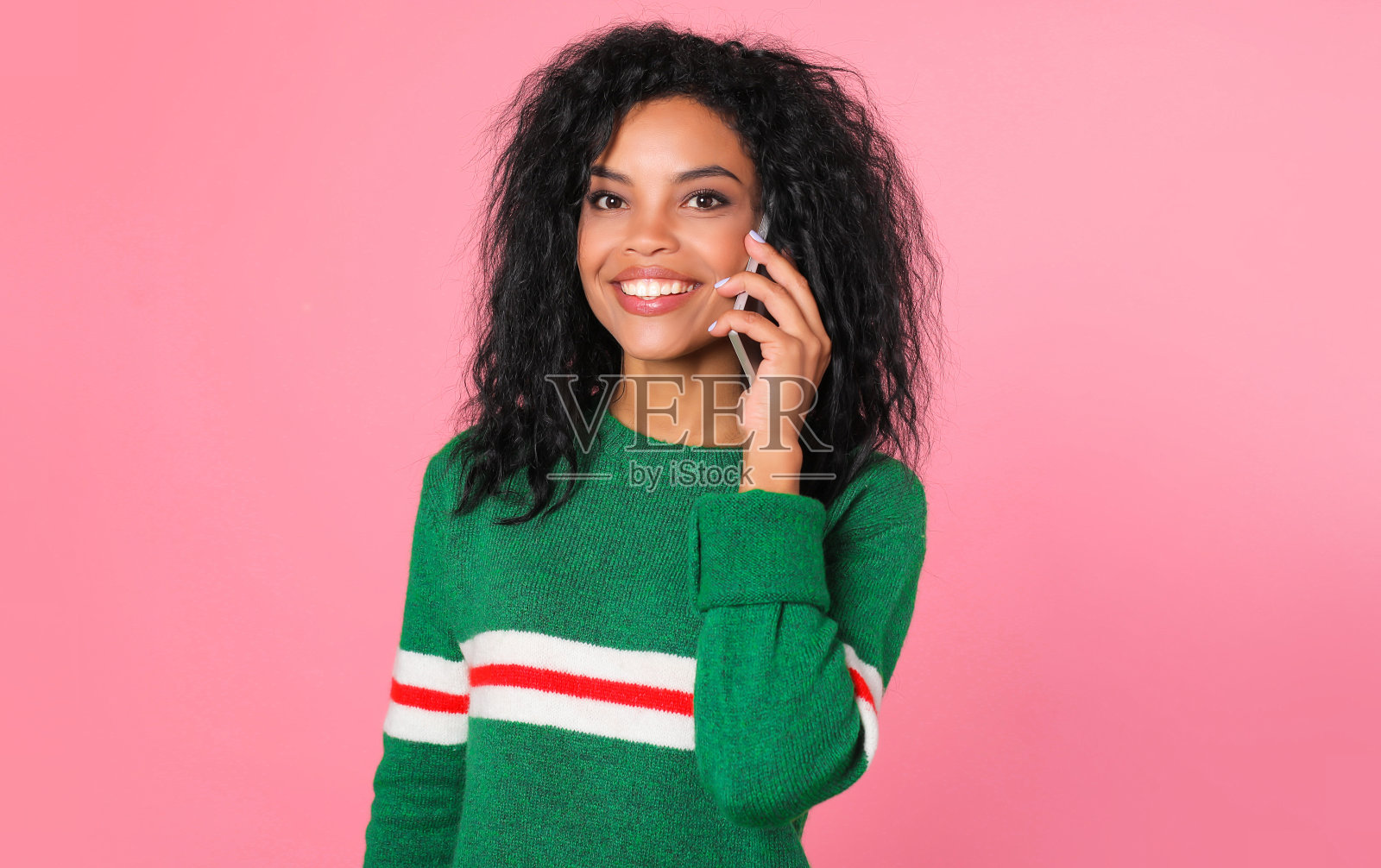 有很多可以聊的。一个忙碌的非洲裔美国女孩穿着一件红白相间的绿色毛衣看着镜头，一边聊着电话一边咧嘴笑着。照片摄影图片