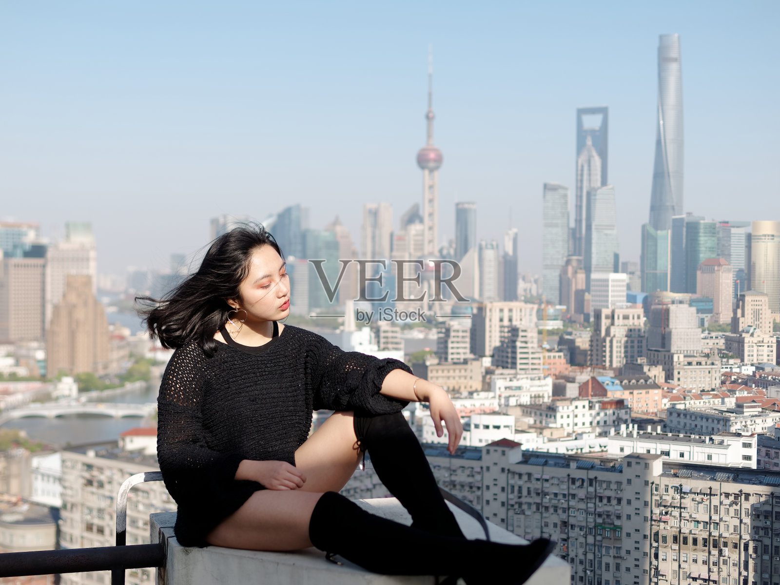 美丽的年轻女子坐在大厦屋顶享受微风，背景模糊的上海外滩标志性建筑。情感、人、美、生活理念。照片摄影图片