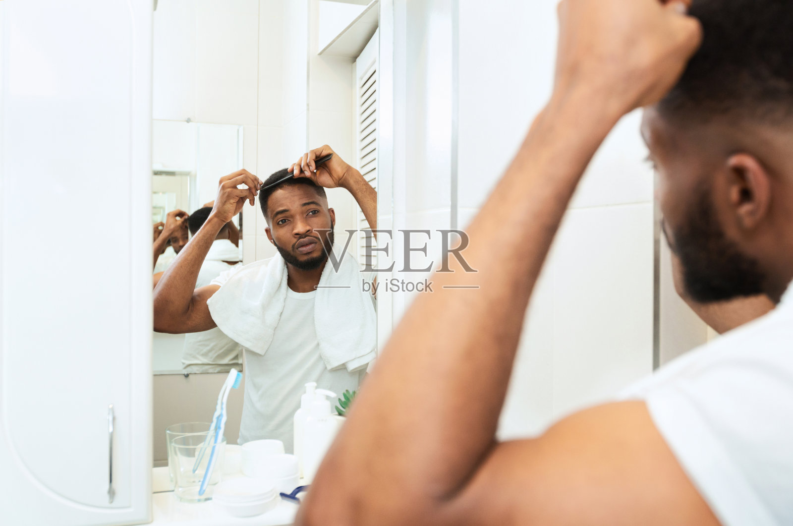 一个年轻的黑人正在检查他的头发，看着浴室的镜子照片摄影图片
