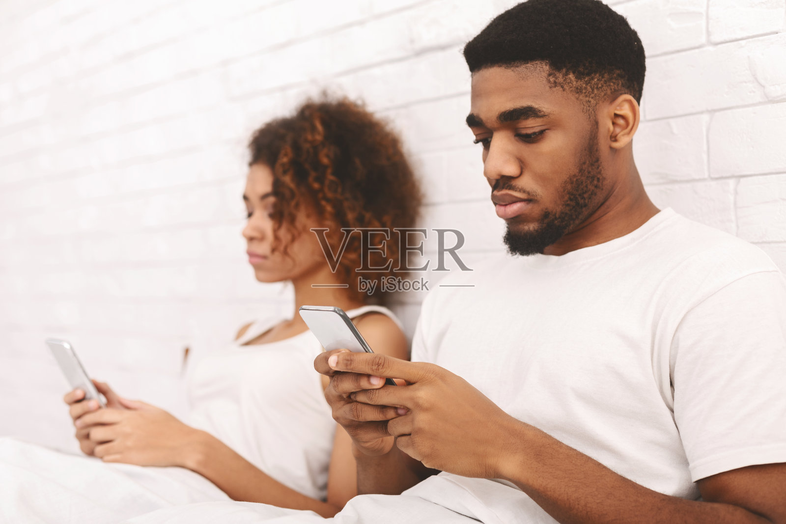 一对黑人情侣在床上用手机，无视对方照片摄影图片