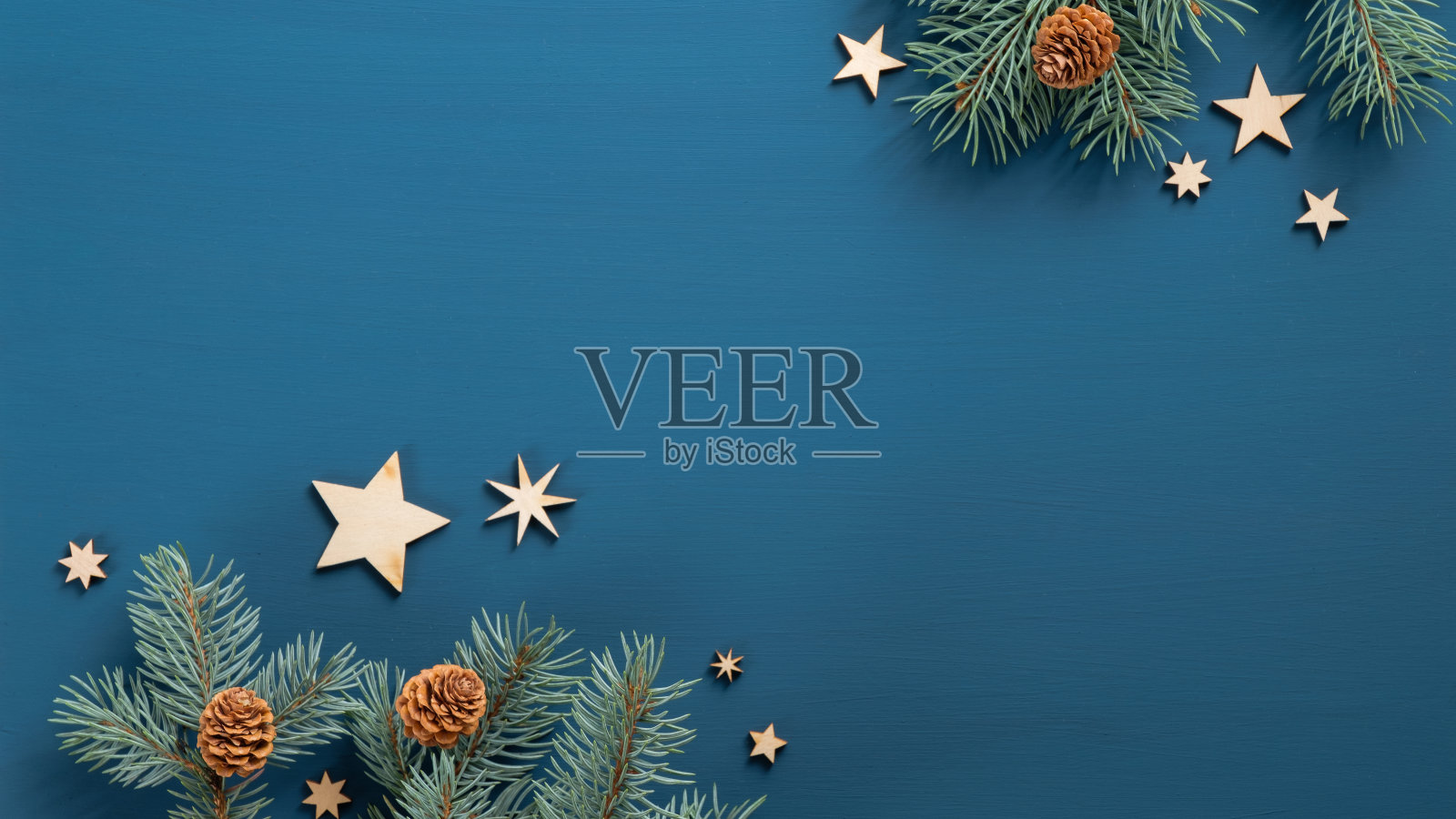 在蓝色背景上平铺着带有锥形和木制的复古星星的圣诞树树枝。前视图。圣诞横幅模型与复制空间，贺卡模板。照片摄影图片