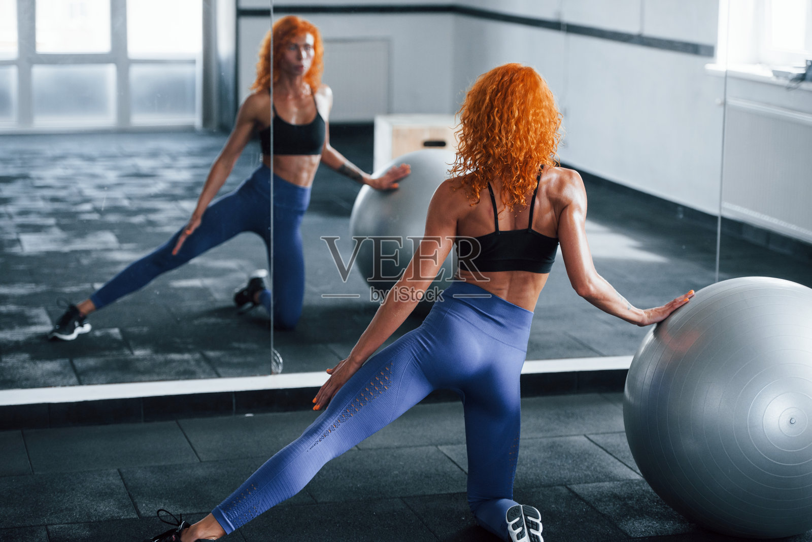 使用银色的健身球。喜欢运动的红发女孩白天去健身房健身。肌肉发达的身体类型照片摄影图片