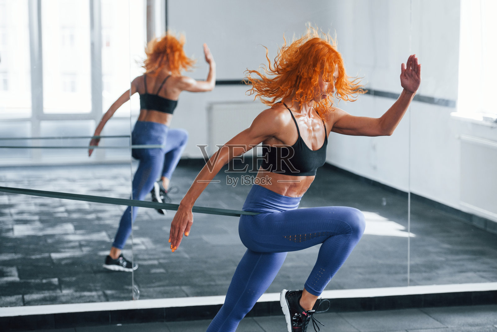 跑到镜子旁边。喜欢运动的红发女孩白天去健身房健身。肌肉发达的身体类型照片摄影图片
