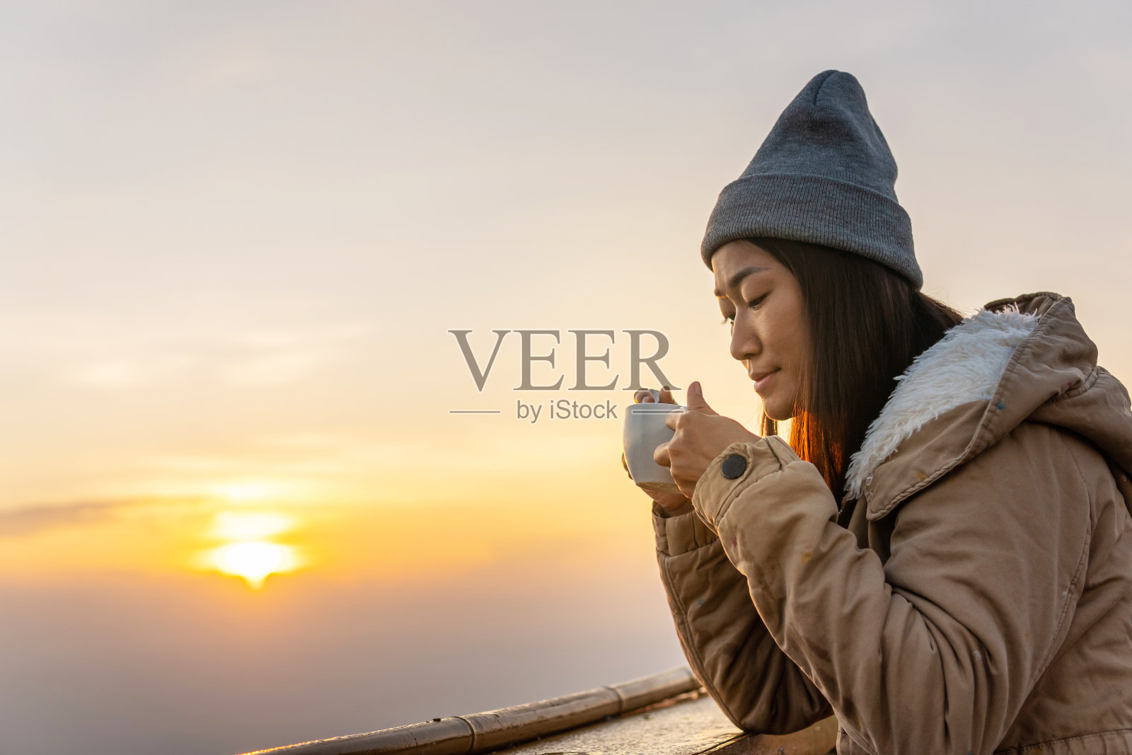 日出时分，一位亚洲妇女坐在山顶上喝咖啡。照片摄影图片