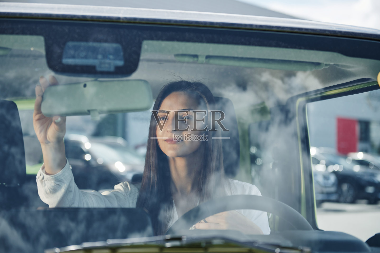 云在玻璃上的反射。在城市中驾驶现代新车的女人的正面视图照片摄影图片