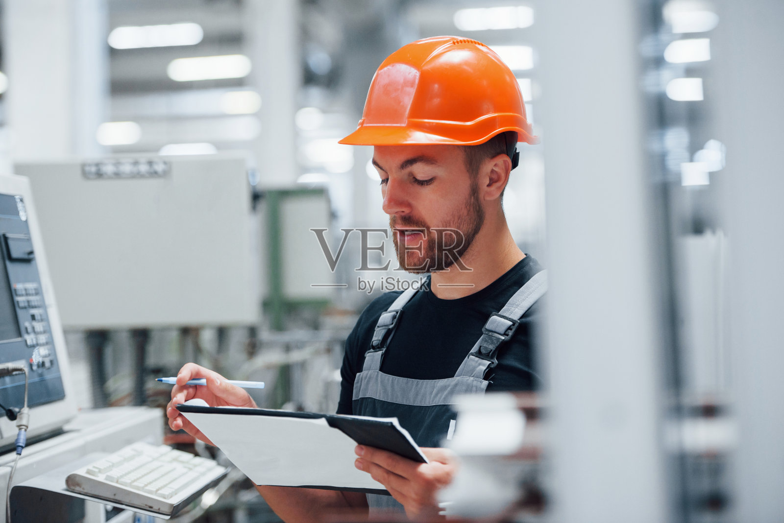 做笔记。工厂内的工业工人。戴着橙色安全帽的年轻技术员照片摄影图片