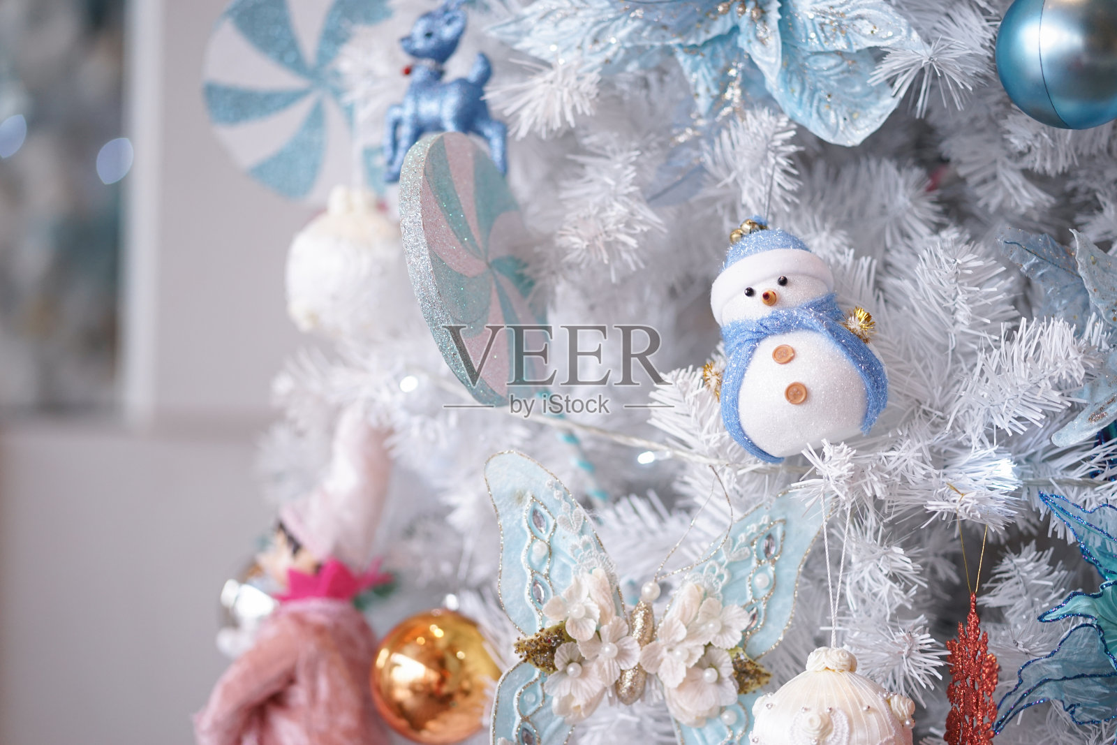 圣诞装饰品。这是一幅白色圣诞树上圣诞装饰的特写，以一个戴着蓝色围巾的雪人为焦点。照片摄影图片