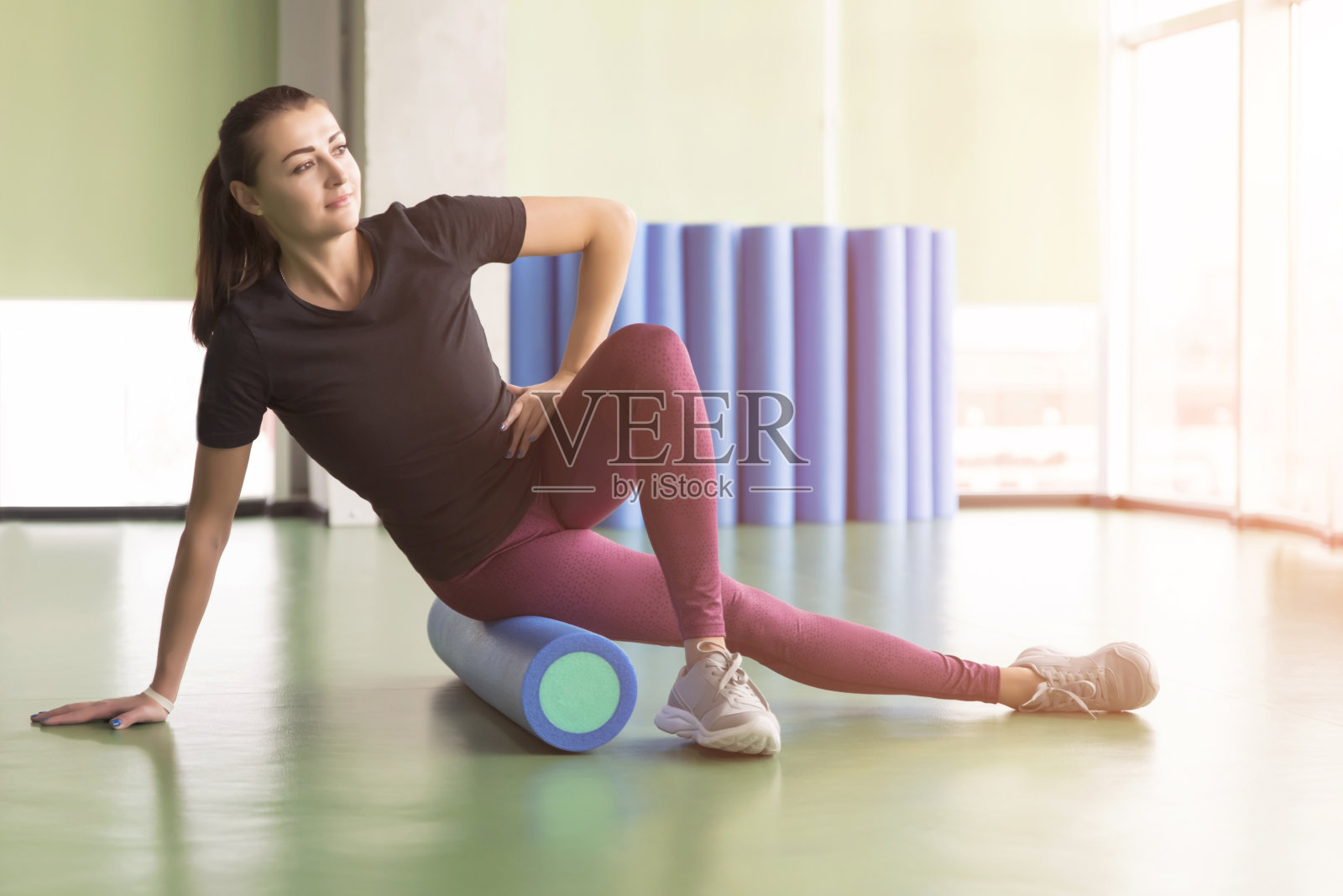 迷人的女性做泡沫滚轮运动和摆姿势在现代明亮健身中心照片摄影图片