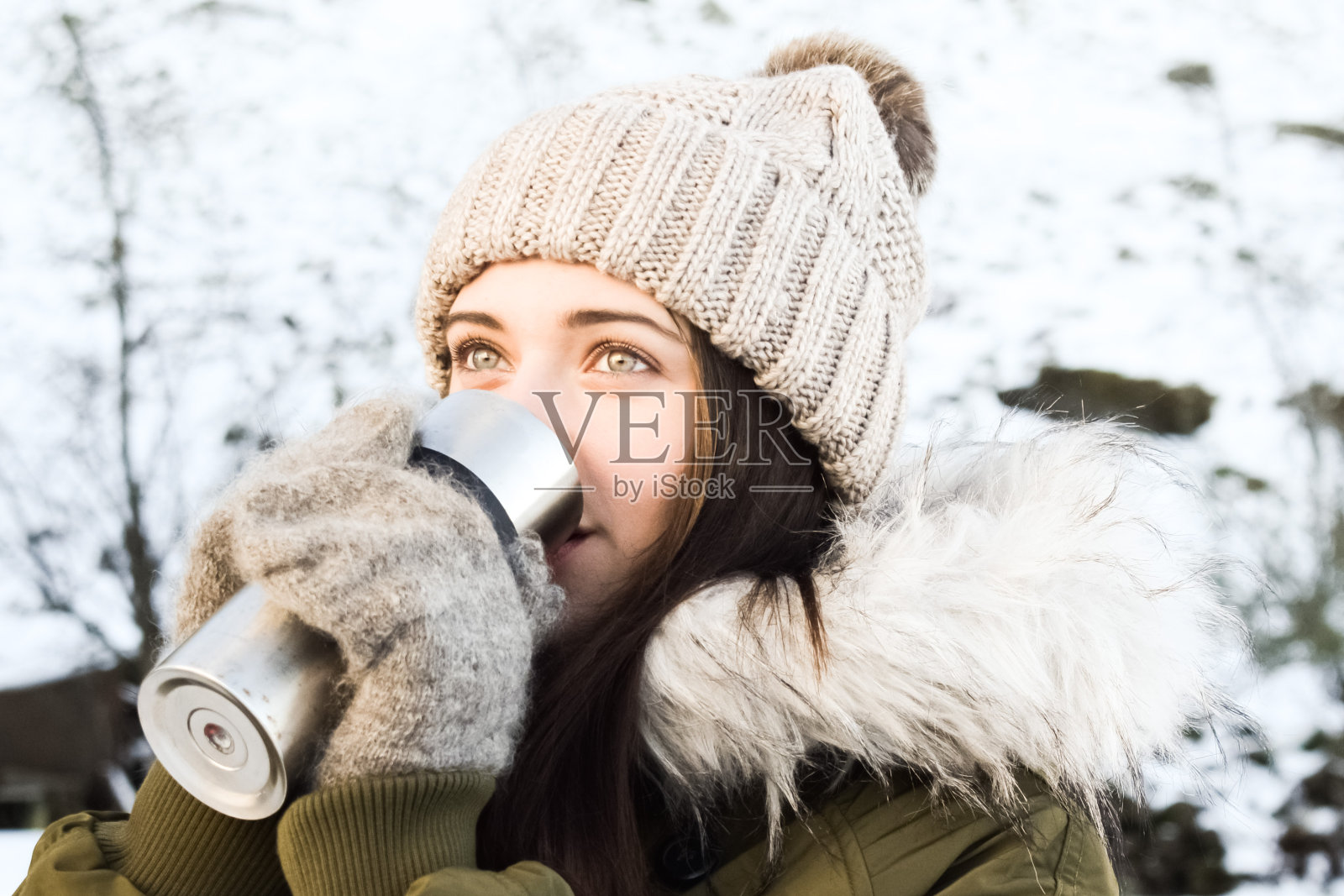 在一个冬天的公园里，一个年轻的女人正在用热水杯喝热饮。照片摄影图片