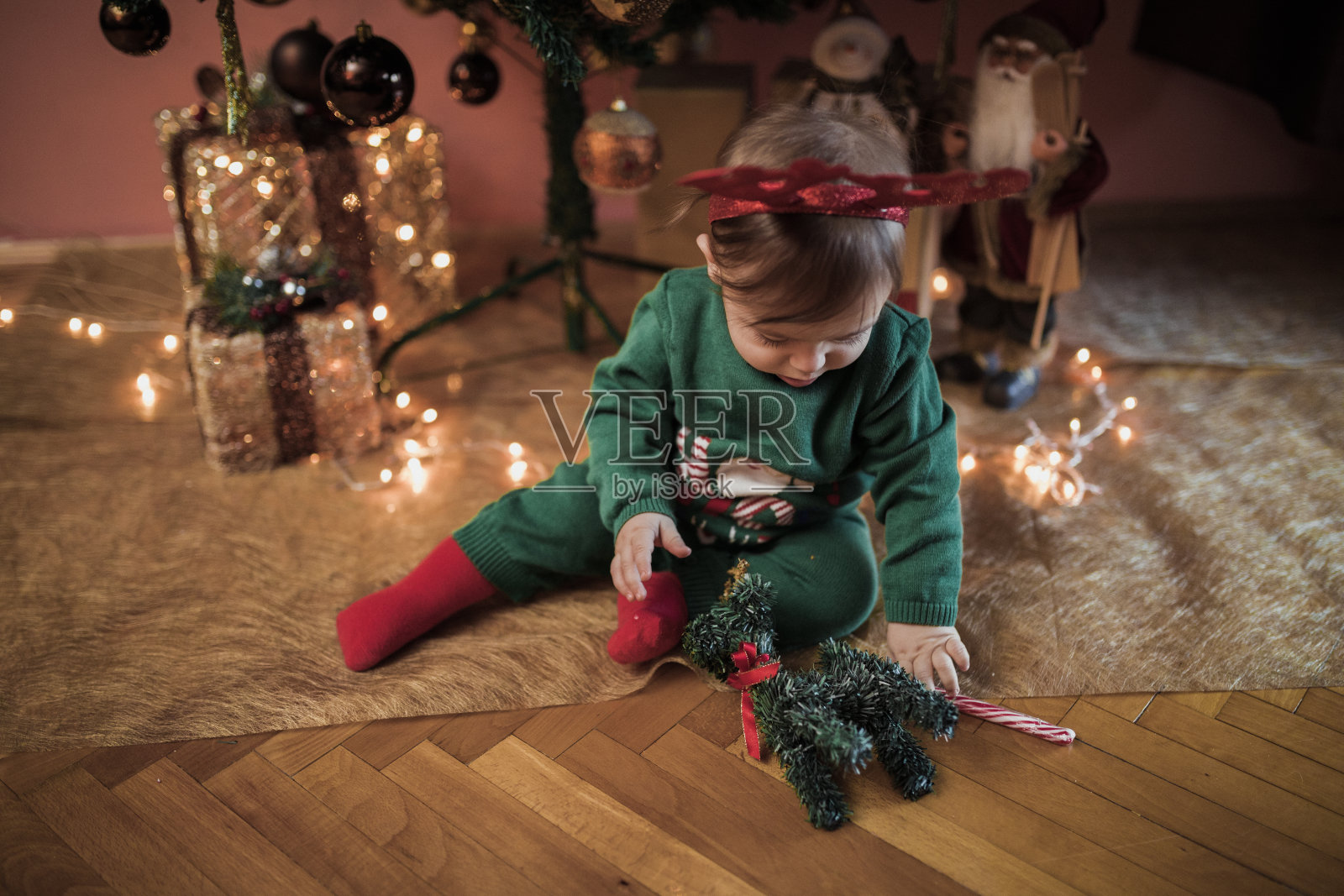 戴着驯鹿角的小男孩坐在圣诞树下照片摄影图片