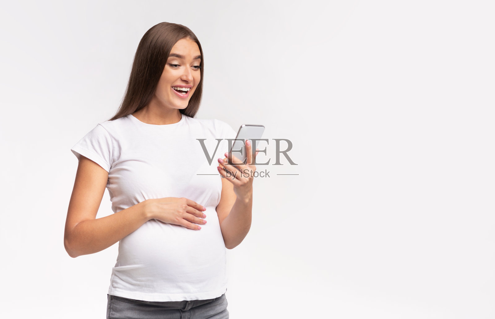 快乐的孕妇站在白色的工作室背景下使用智能手机照片摄影图片