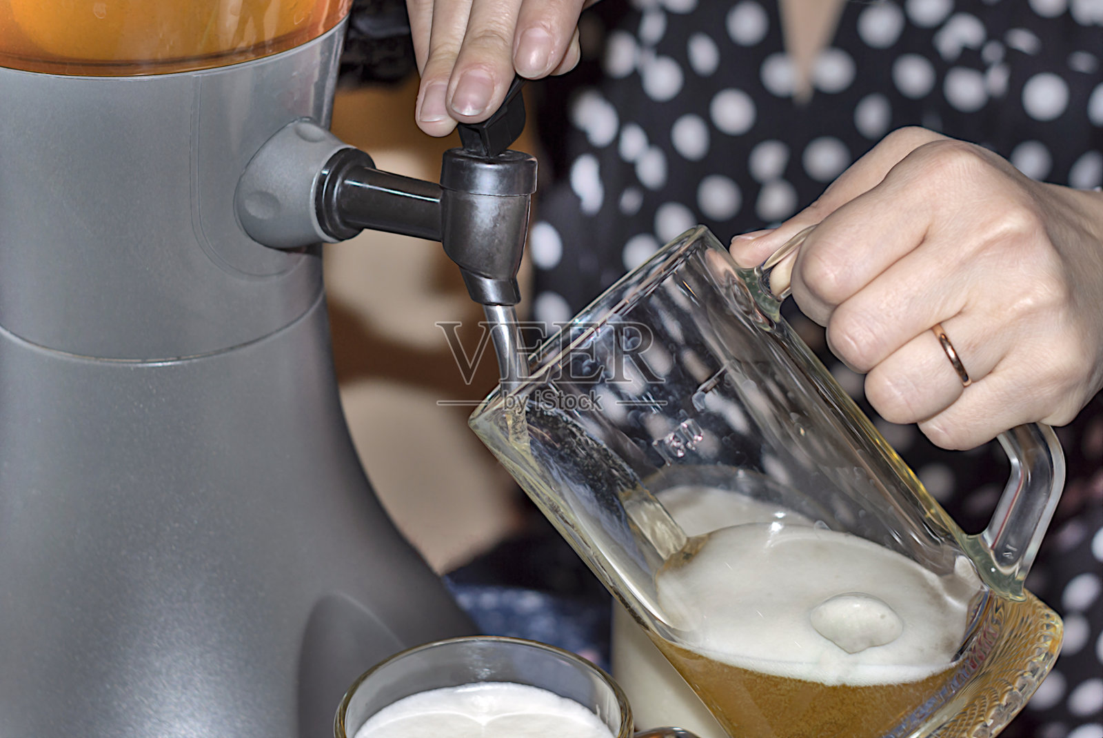 女人从桌上的冷饮器里把新鲜的冰啤酒倒进啤酒杯里照片摄影图片