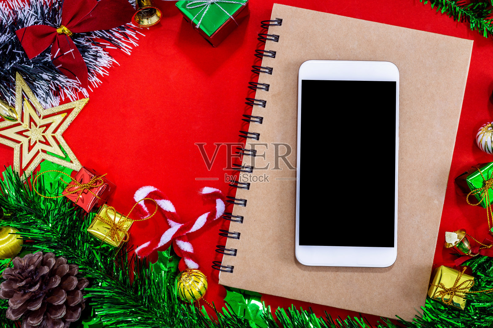 俯视图图像的圣诞节日装饰与空的智能手机，笔记本和铅笔在红纸的背景，新年的概念。照片摄影图片