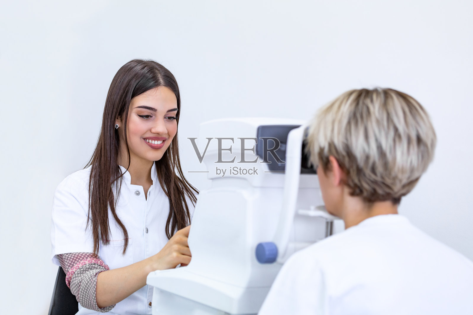 在现代诊所里，女医生眼科医生正在检查漂亮年轻女子的眼睛视力。眼科门诊的医生和病人。照片摄影图片