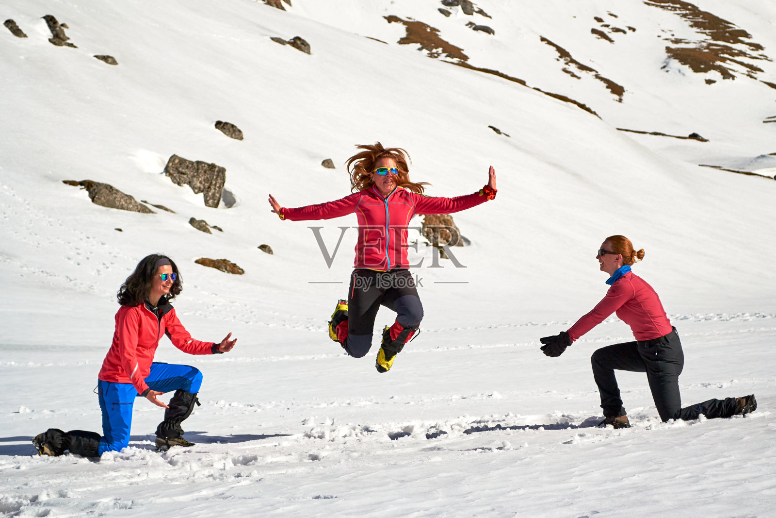三名女徒步旅行者在罗马尼亚布塞吉山的雪中玩耍和跳跃。照片摄影图片