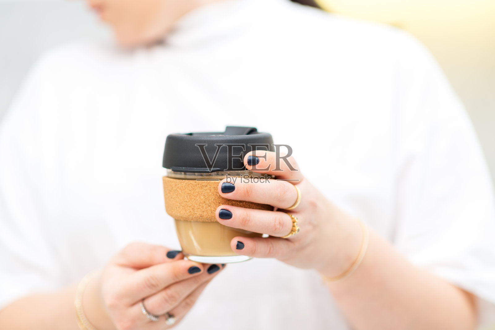 一个面无表情的女人拿着可重复使用的外带玻璃咖啡杯。照片摄影图片