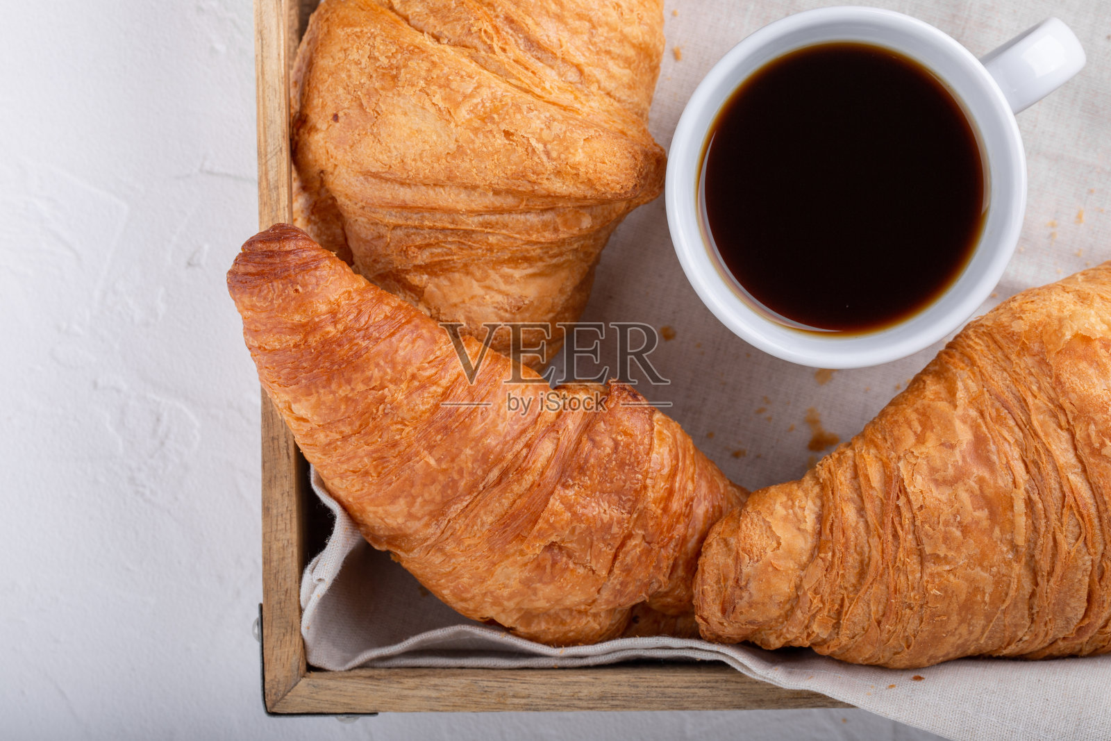 一杯咖啡羊角面包放在木托盘上。白色餐桌上的节日早餐。顶视图,特写。照片摄影图片
