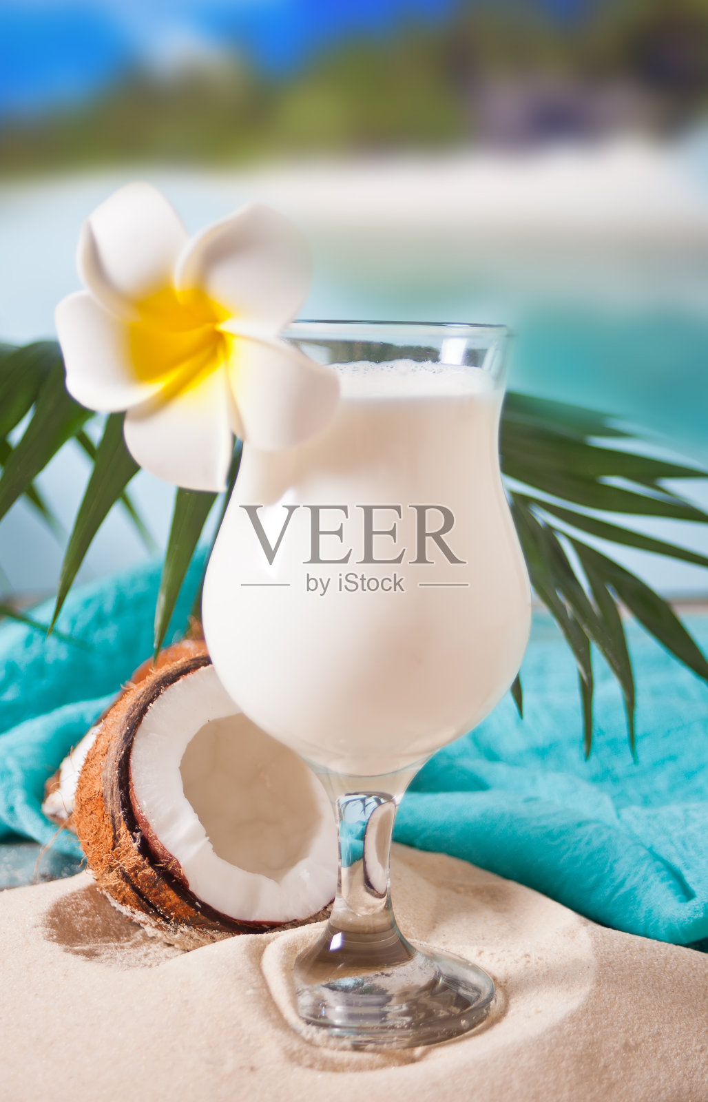 传统的加勒比异国情调的热带鸡尾酒饮菠萝朗姆酒在一个玻璃杯与鸡蛋花，棕榈叶和椰子的背景。热带海滩野餐概念。照片摄影图片