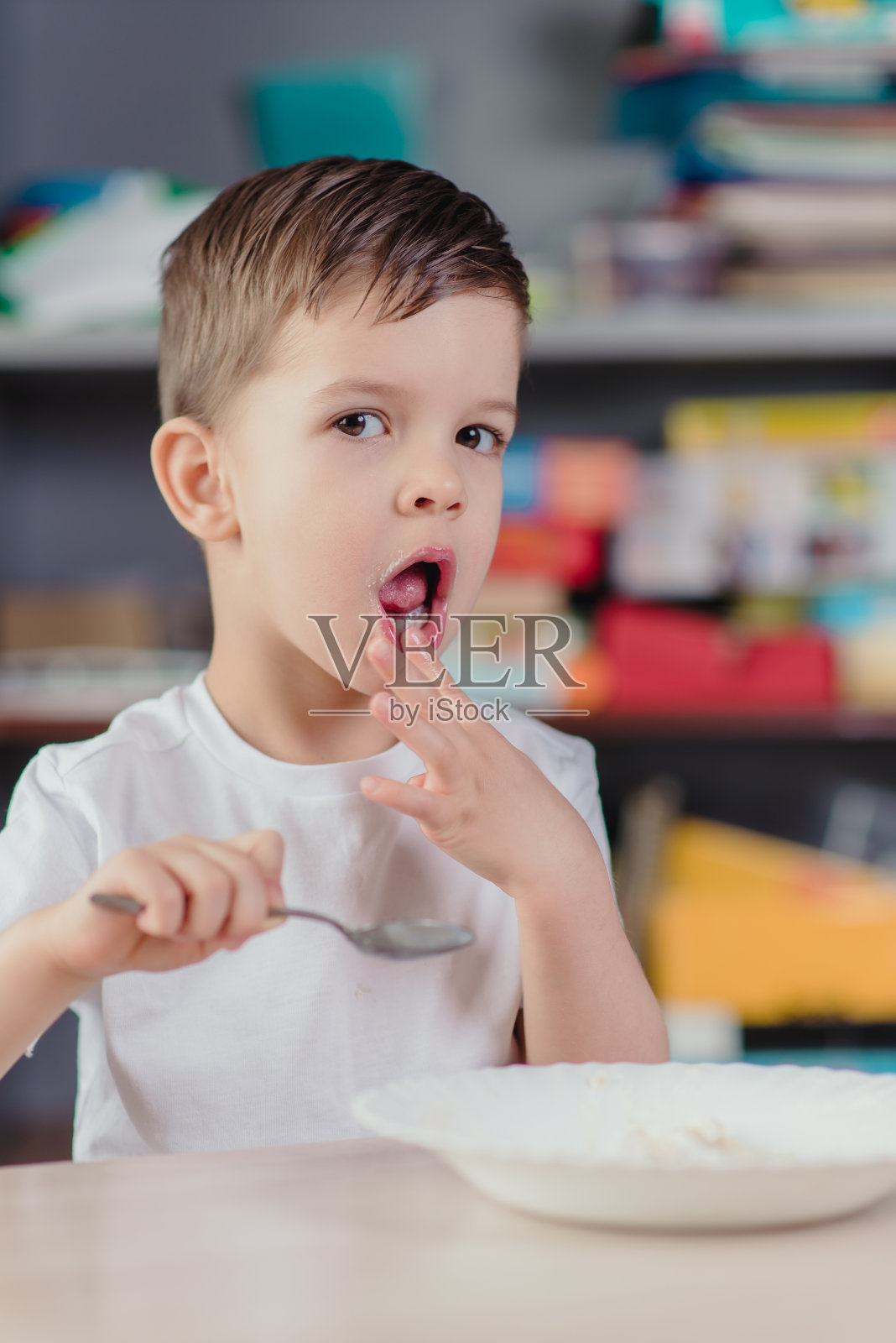 这孩子早餐吃燕麦粥。这个男孩坐在家里厨房的桌子旁吃东西。照片摄影图片