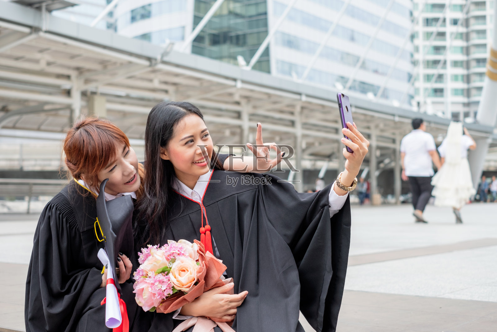 两个年轻的女孩用手机拍照庆祝一个毕业的单身汉照片摄影图片