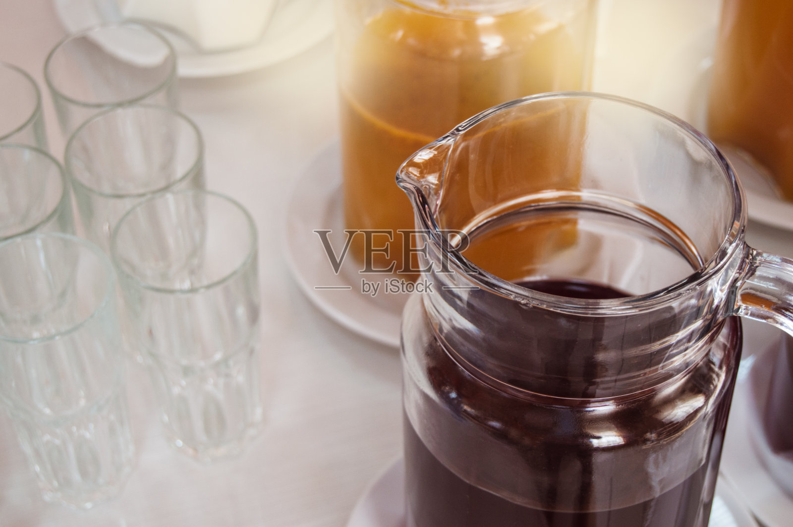 在酒店的早餐，满的玻璃壶和凉爽的软饮料，果汁，空的玻璃杯，早上的阳光照片摄影图片