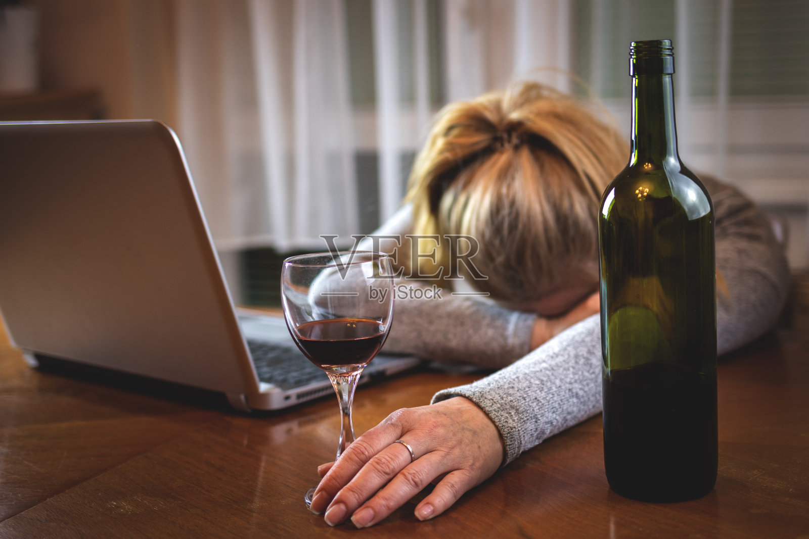 醉酒的女人喝酒后拿着打开的笔记本电脑睡在桌子上照片摄影图片