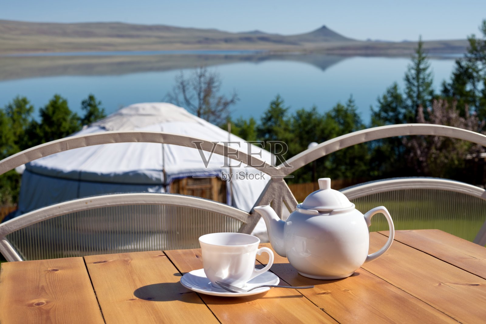 在一个阳光明媚的夏日早晨，湖边的桌子上放着一个茶杯茶壶，背景是一个亚洲毡房。照片摄影图片