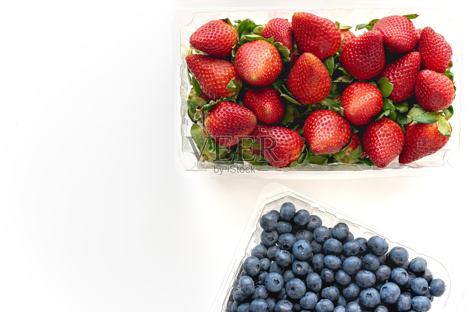 草莓和蓝莓在塑料容器靠近白色背景，从上面看照片摄影图片