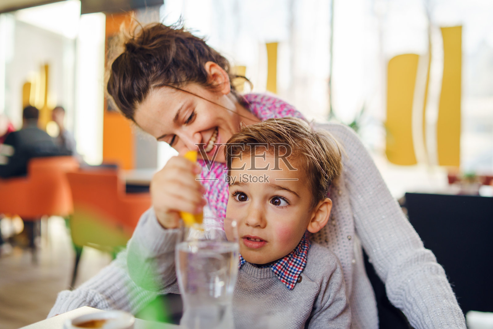 小三岁白人男孩的肖像和他的母亲坐在桌子旁年轻的女人在咖啡馆喝着一杯柠檬水制作柠檬汁照片摄影图片