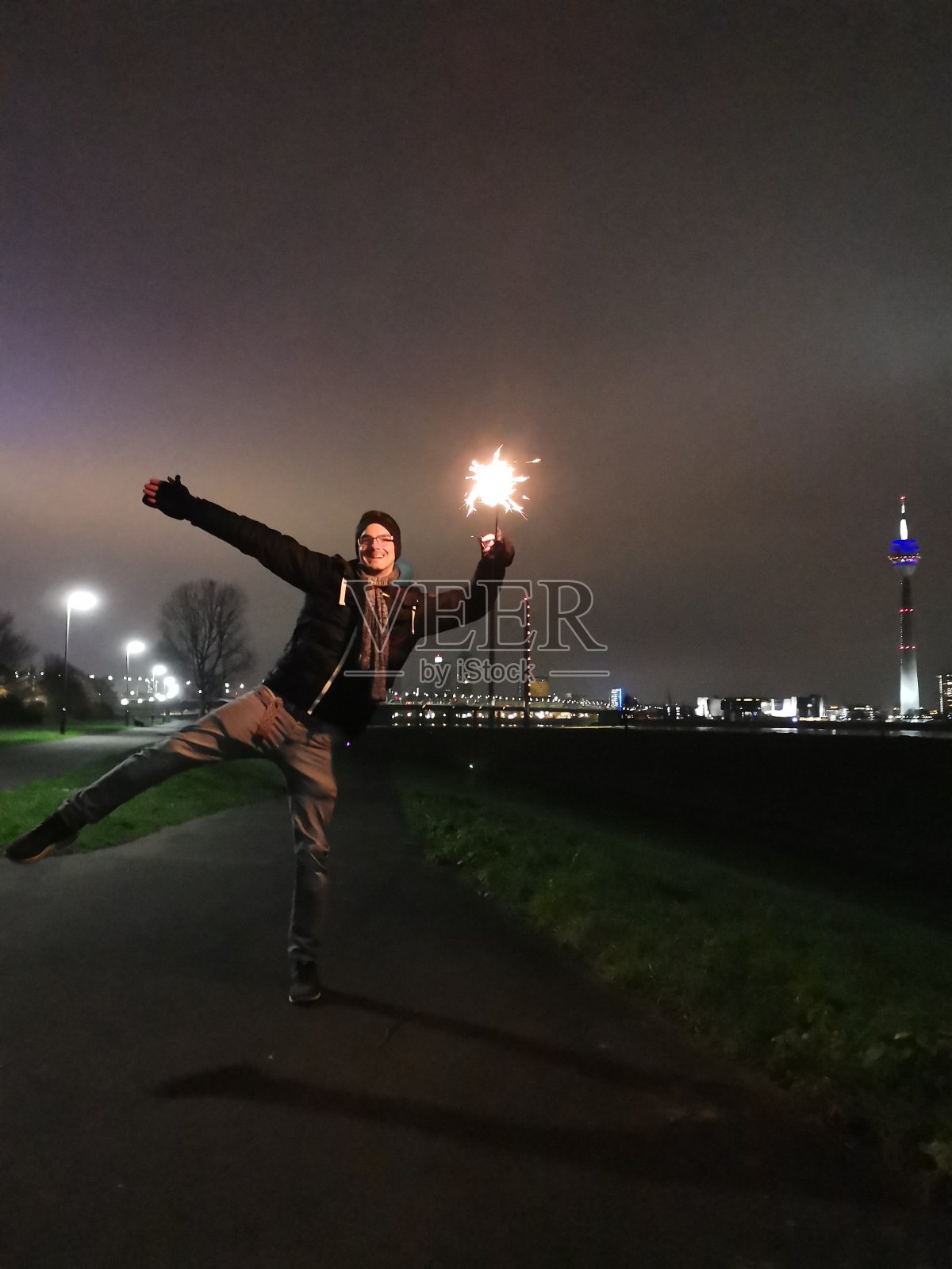 一个年轻人晚上在Düsseldorf' skyline前拿着闪闪发光的东西摆造型照片摄影图片