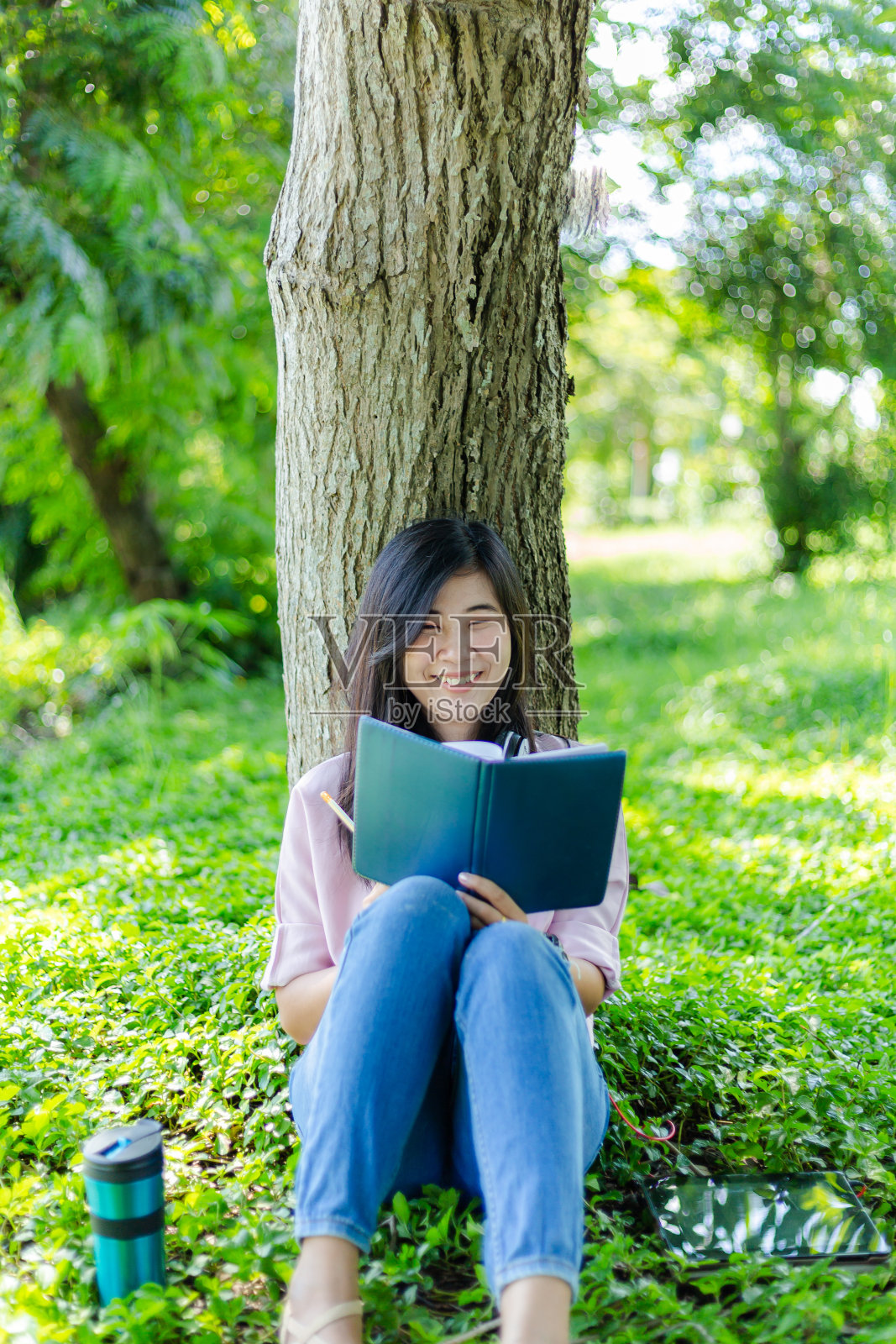 一个年轻或十几岁的亚洲女孩学生在大学微笑和阅读的书，看平板电脑或笔记本电脑在暑假。照片摄影图片