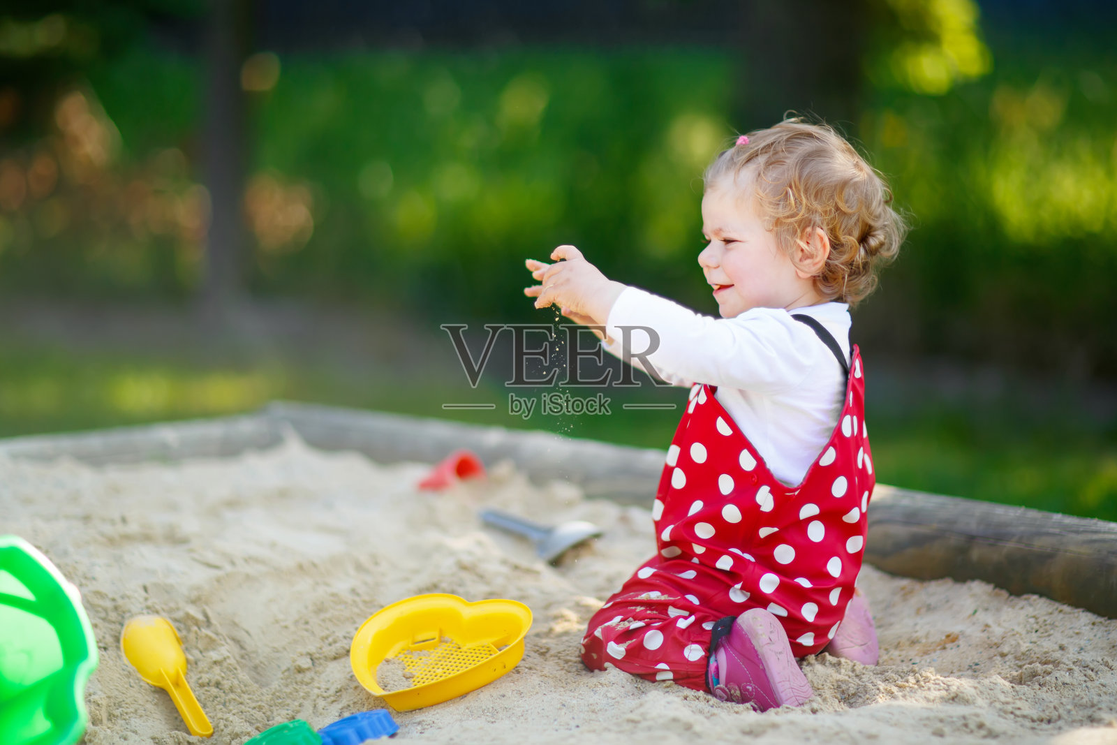 可爱的蹒跚学步的小女孩在户外操场上玩沙子。美丽的婴儿在红色的口香糖裤子有乐趣在阳光明媚温暖的夏天。孩子有五颜六色的沙玩具。健康活泼的宝宝在户外玩游戏照片摄影图片