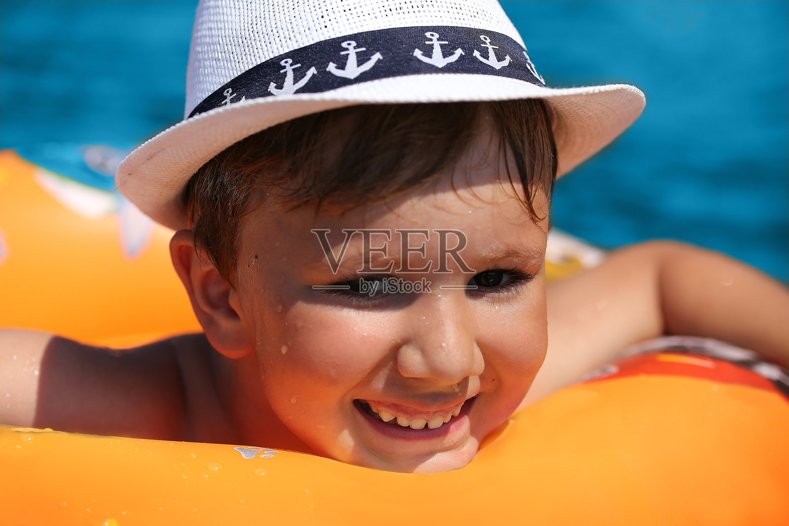 快乐的孩子在一个橙色的充气圈上漂浮在蓝色的海面上，围绕着浪花照片摄影图片