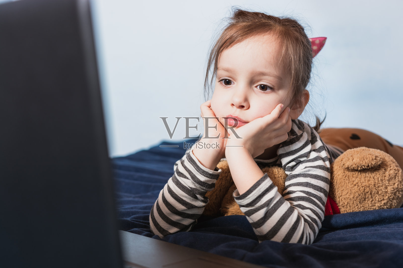 孩子躺在床上使用笔记本电脑。照片摄影图片