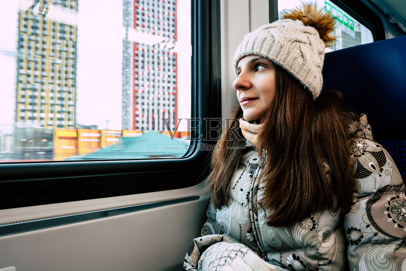 肖像迷人的年轻女子身穿米色温暖针织帽与毛皮绒球和围巾。女孩透过火车车窗看风景，享受旅行照片摄影图片