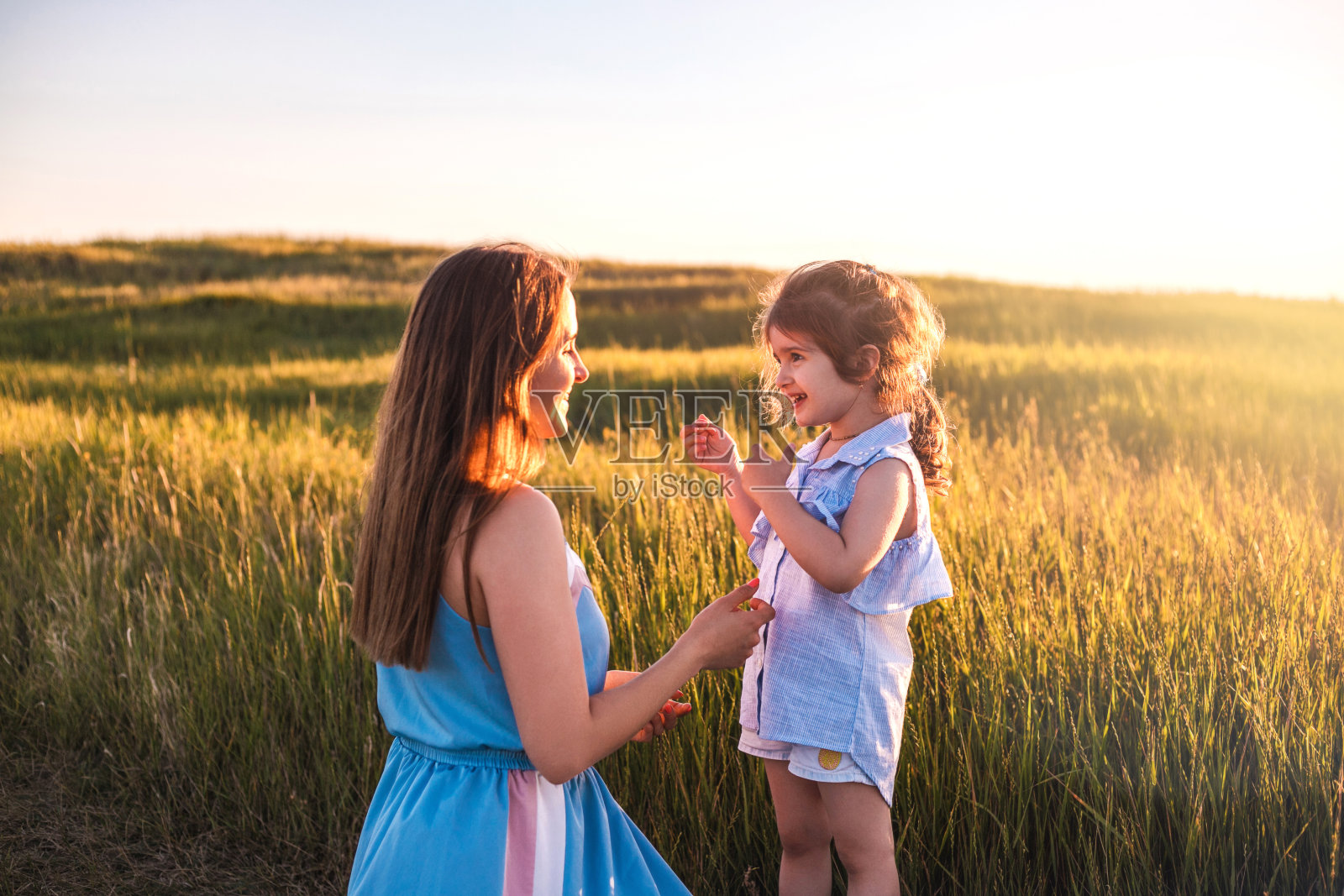 年轻的母亲和女儿，拥抱和玩耍在金色的阳光田野。照片摄影图片
