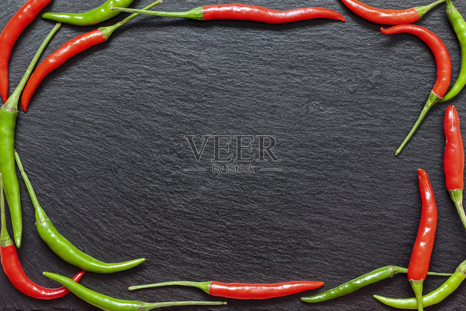 新鲜辛辣的红椒和青椒在石板上，各种彩色的辣椒和辣椒在黑色的背景从上面。俯视图，复制空间。照片摄影图片