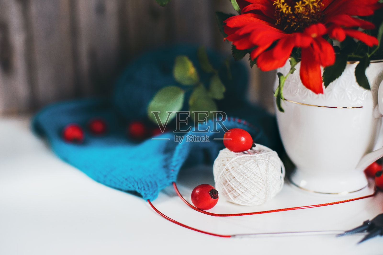 花瓶里放着一束玫瑰和红花，毛线球、针、针织品，放在舒适的白色桌子上。照片摄影图片
