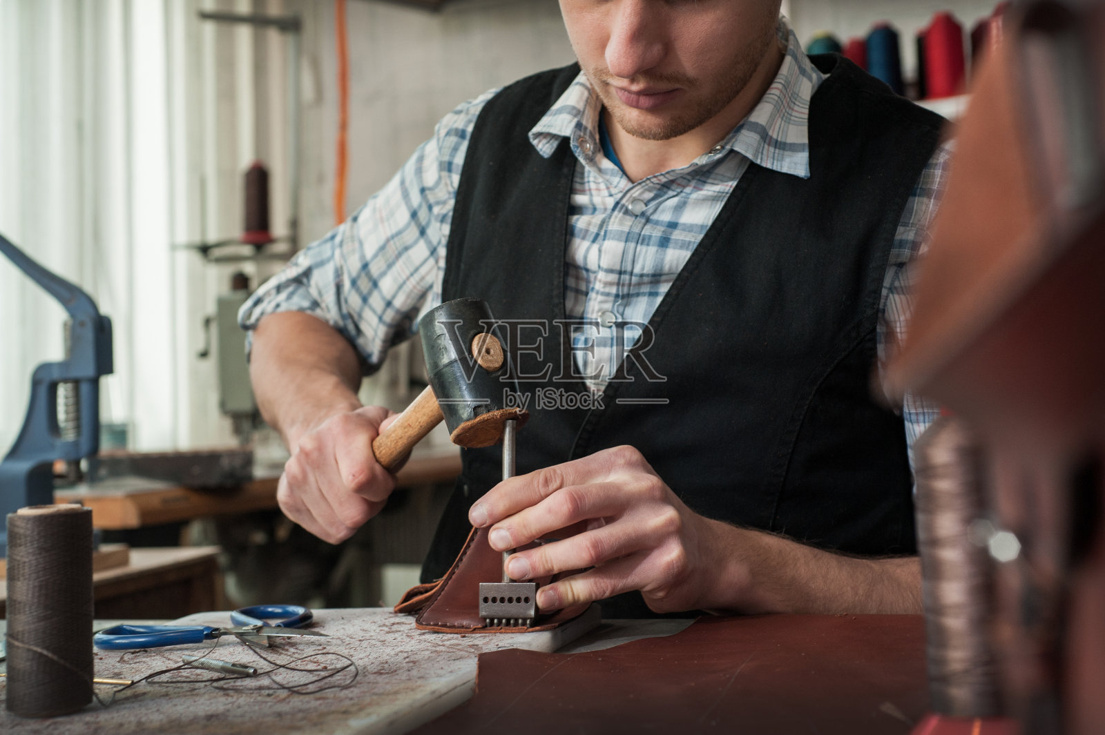 皮革工匠使用锤子与天然皮革工作的特写。照片摄影图片