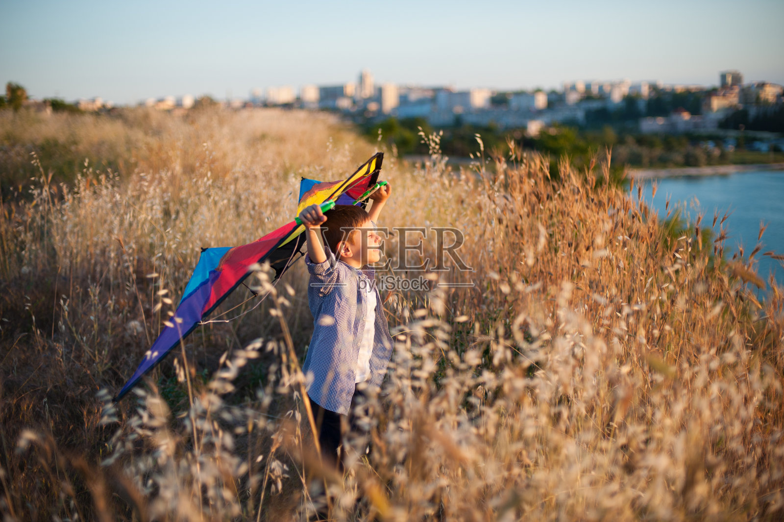 幸福梦幻的小高加索男孩闭着眼睛拿着风筝站在海边和城市附近的田野照片摄影图片