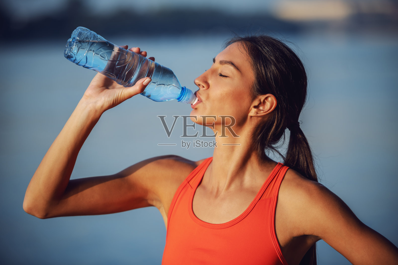 侧面吸引苗条口渴的女运动员饮用新鲜的水从瓶子。照片摄影图片