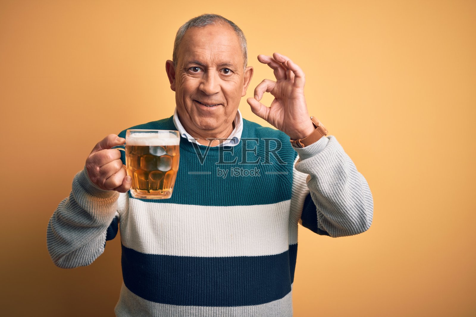 高级英俊男子喝啤酒罐站在孤立的黄色背景微笑积极做ok手势与手和手指。成功的表达。照片摄影图片