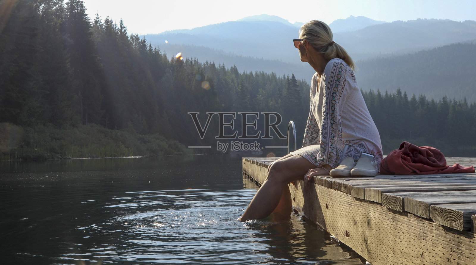成熟的女人在木栈桥上休息，眺望湖面照片摄影图片