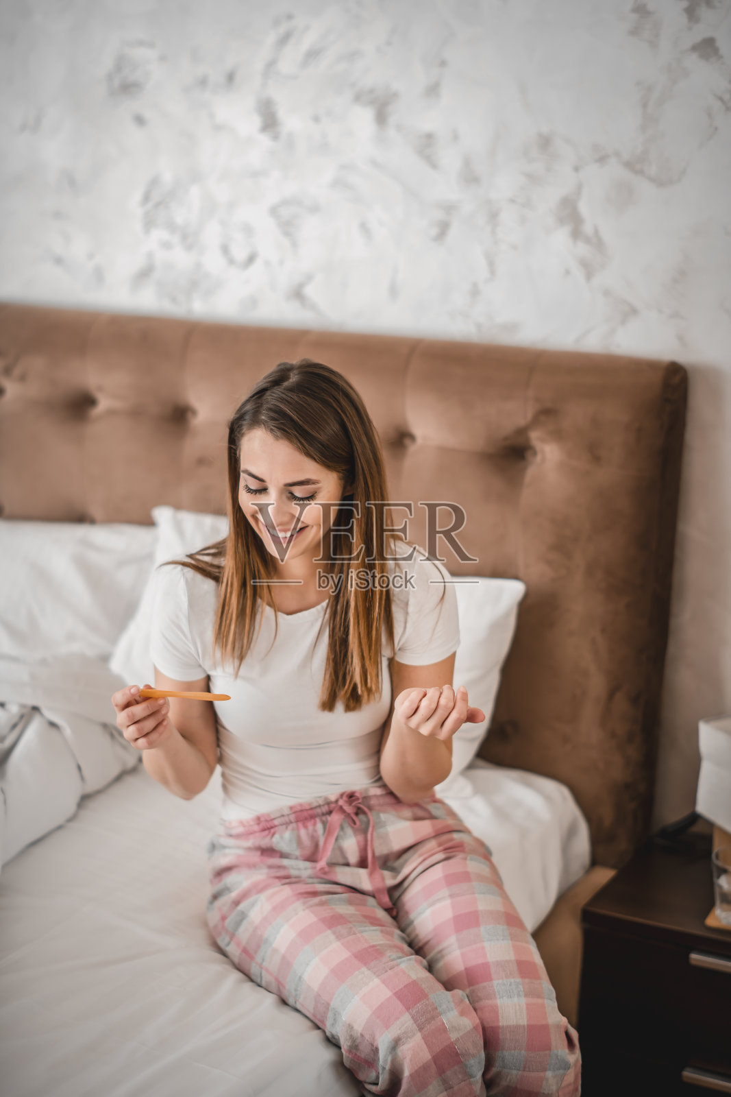 微笑的年轻女子坐在床上，拿着验孕棒照片摄影图片
