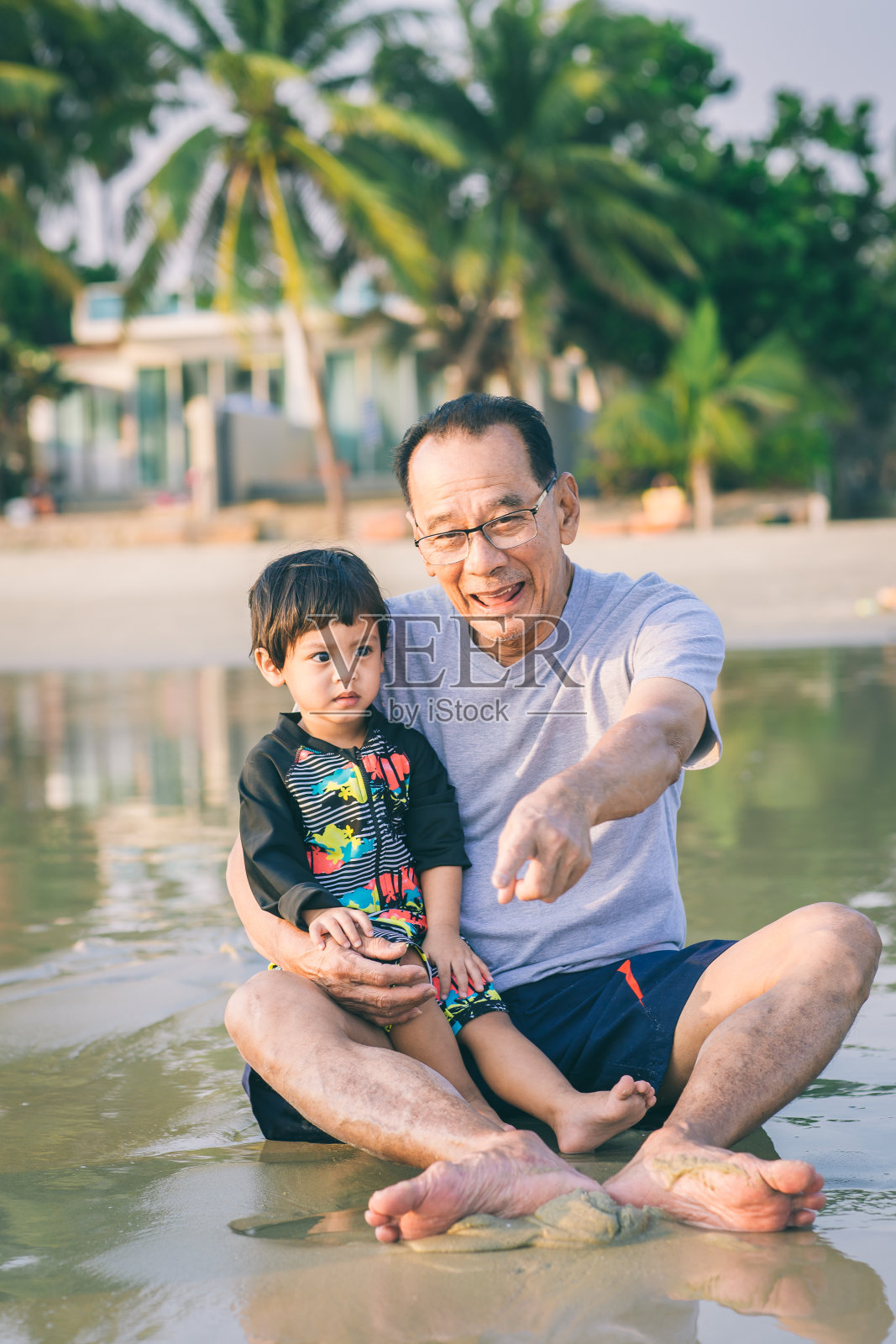 一家人在海滩上玩耍。夏天，父母和孩子们在海滩上放松。幸福健康的家庭，爷爷和侄子在沙滩上建造沙堡，面带微笑，无忧无虑。照片摄影图片