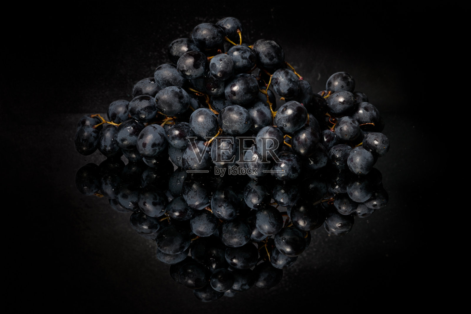 一串深色的黑葡萄放在一张深色的镜子桌上。照片摄影图片